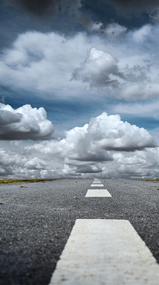 Paved Road with blue skies and fluufy clouds